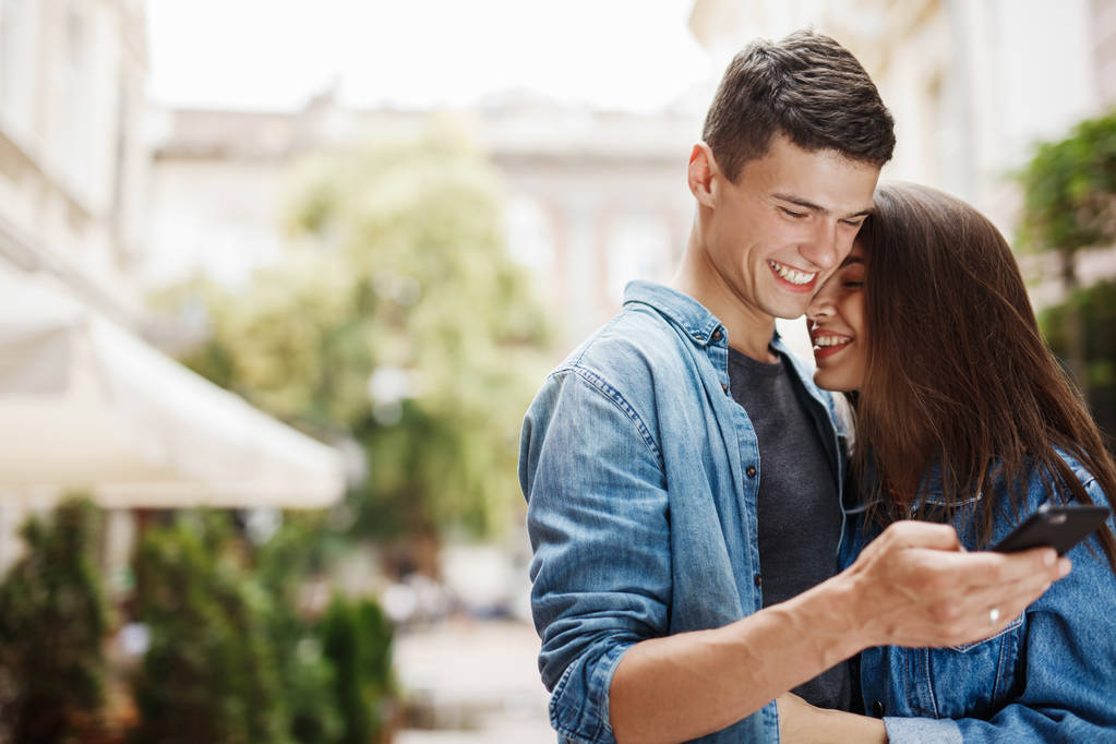 Couple or friends laughing funny and having fun with a smart phone in a big city street - Photo, Image