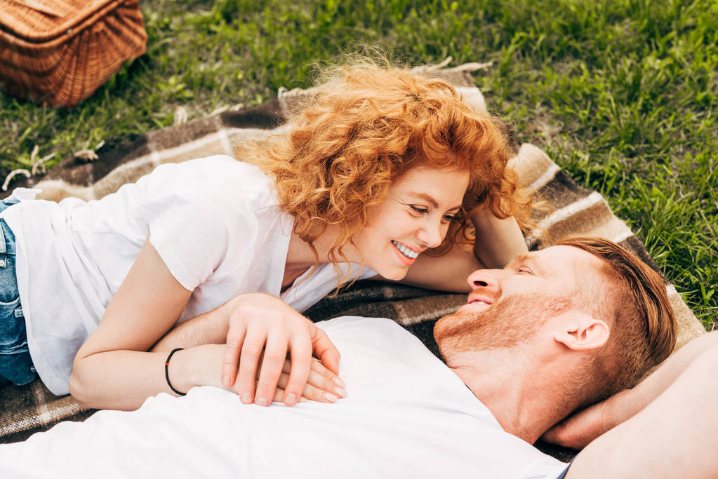 χαρούμενος νεαρός κοκκινομάλλα ζευγάρι ξαπλωμένο στο καρό και κάθε άλλο χαμογελάει πικ-νικ - Φωτογραφία, εικόνα