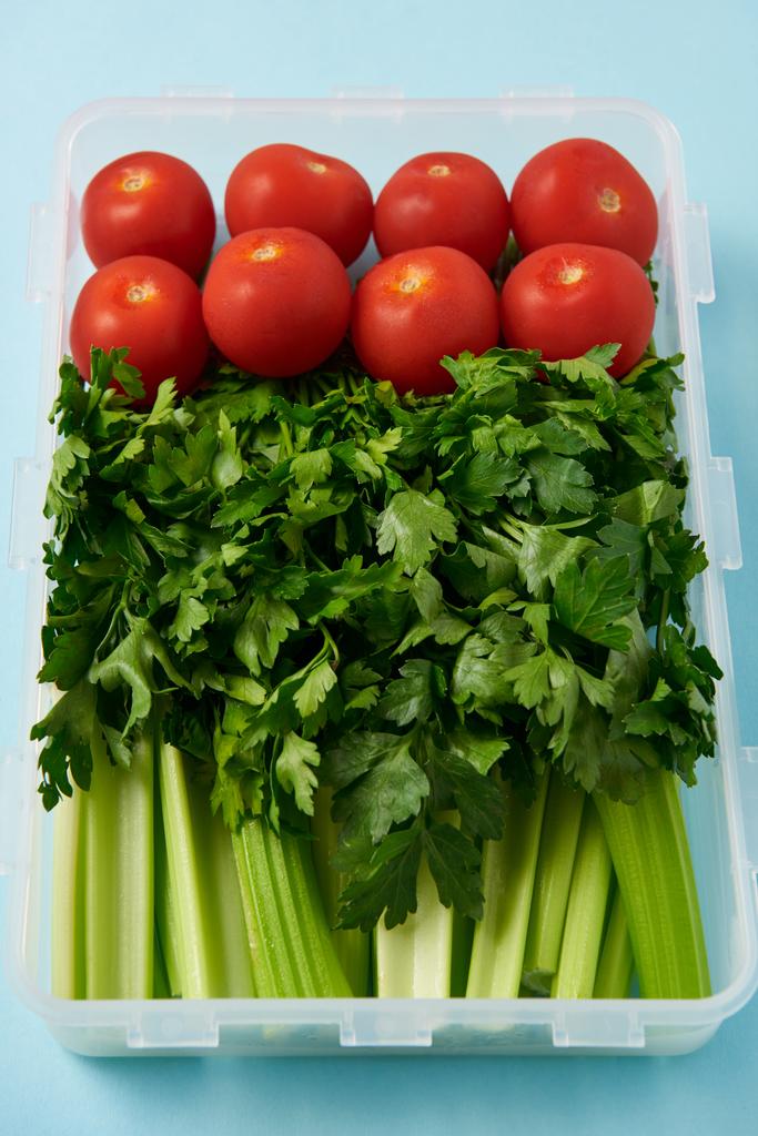 vue rapprochée du récipient alimentaire rempli de tomates fraîches, de persil et de céleri sur fond bleu
 - Photo, image