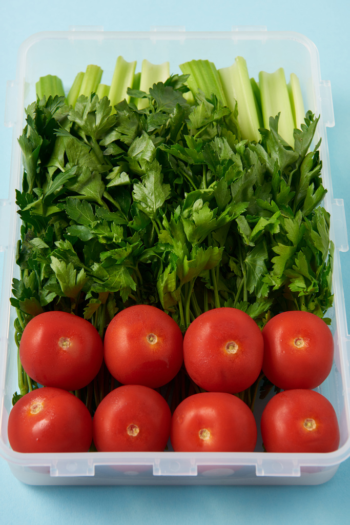 close up view of food container full of fresh tomatoes, parsley and celery on blue background - Photo, Image