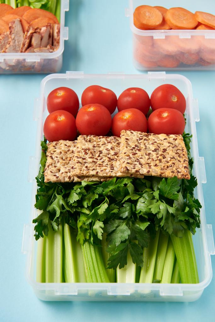 vista de cerca de la disposición de recipientes de alimentos llenos de verduras saludables, rebanadas de carne y galletas en el fondo azul
 - Foto, Imagen