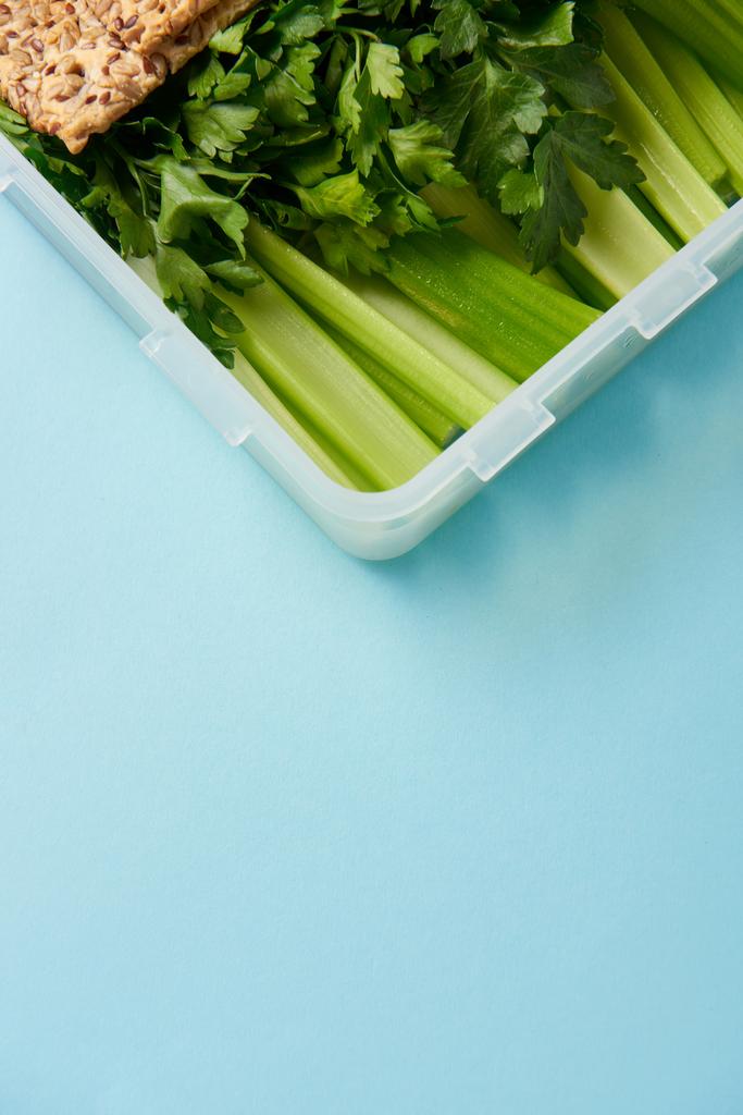 primer plano vista de contenedor de alimentos lleno de perejil saludable y apio aislado en azul
 - Foto, Imagen