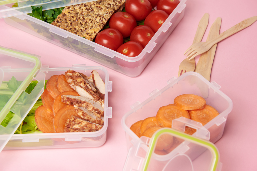 κλείνω πάνω θέα υγιεινών τροφίμων που διοργανώνονται σε δοχεία τροφίμων και τα μαχαιροπήρουνα σε ροζ φόντο - Φωτογραφία, εικόνα