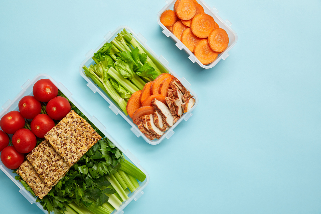 vista superior do arranjo de recipientes de alimentos com legumes saudáveis frescos, carne e biscoitos isolados em azul
 - Foto, Imagem