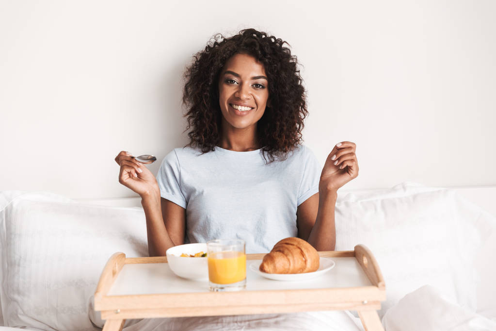 Šťastná mladá Afričanka s chutnou snídaní na zásobník v posteli - Fotografie, Obrázek