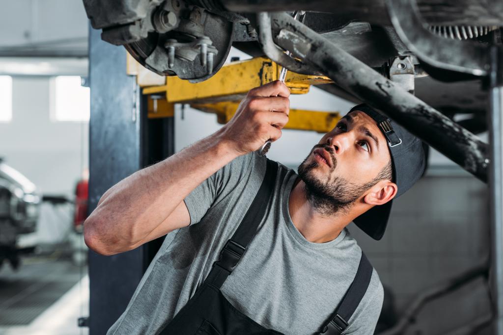 työmies, jolla on laitteet auton korjaamiseen korjaamossa
 - Valokuva, kuva
