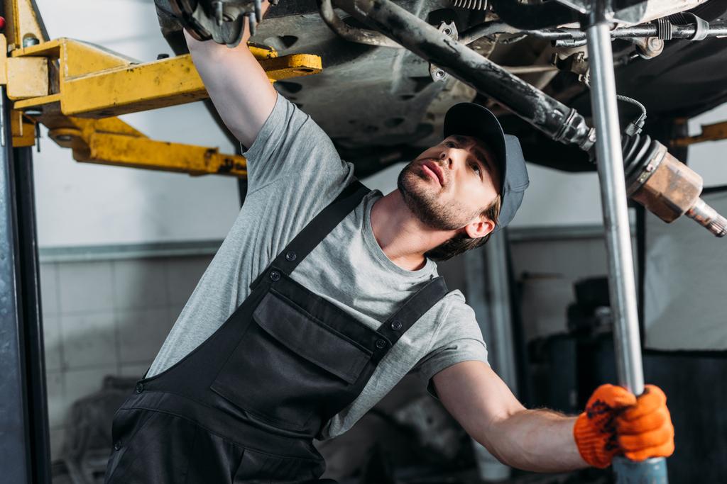 mecânico em uniforme trabalhando com carro na oficina de reparação de automóveis
 - Foto, Imagem
