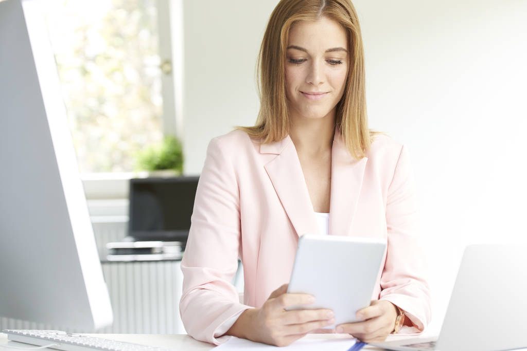 Atraktivní mladá podnikatelka digitální tablet drží v ruce a surfování na internetu, zatímco sedí v kanceláři a práci. - Fotografie, Obrázek