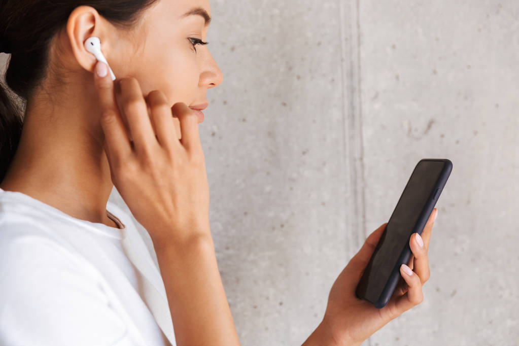 Крупним планом усміхнена азіатка слухає музику з навушниками та мобільним телефоном у приміщенні
 - Фото, зображення