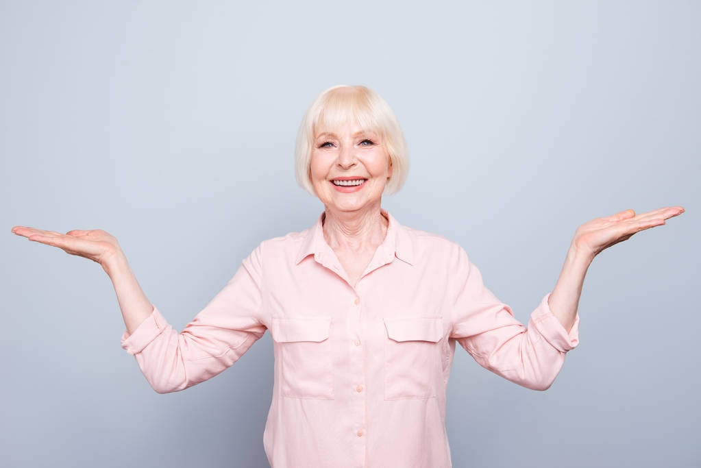 Oude volwassen blonde blij vrolijke dame glimlachen, palmen tonen gebaar met handen, twee kanten, over grijze achtergrond, op zoek recht, geïsoleerd - Foto, afbeelding