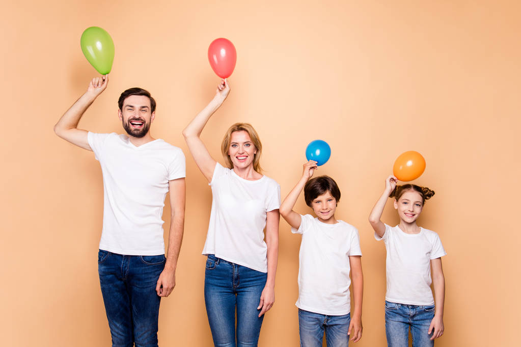 Jovem família sorridente, pai barbudo, mãe loira, menino e menina vestindo jeans azuis e camisetas brancas, de pé em odrer de hierarquia, mantendo bolas de ar acima de suas cabeças
 - Foto, Imagem