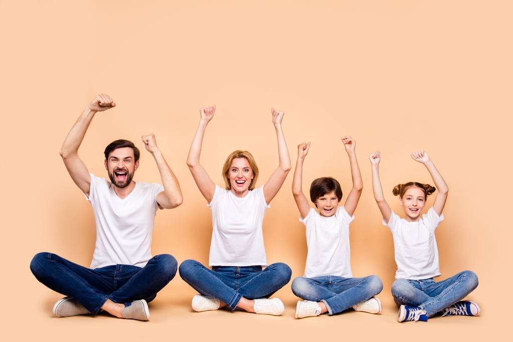Молодая улыбающаяся семья, бородатый отец, мать-блондинка, мальчик и девочка в синих джинсах и белых футболках, сидящие в одрере иерархии в позе лотоса, поднимающие руки
 - Фото, изображение