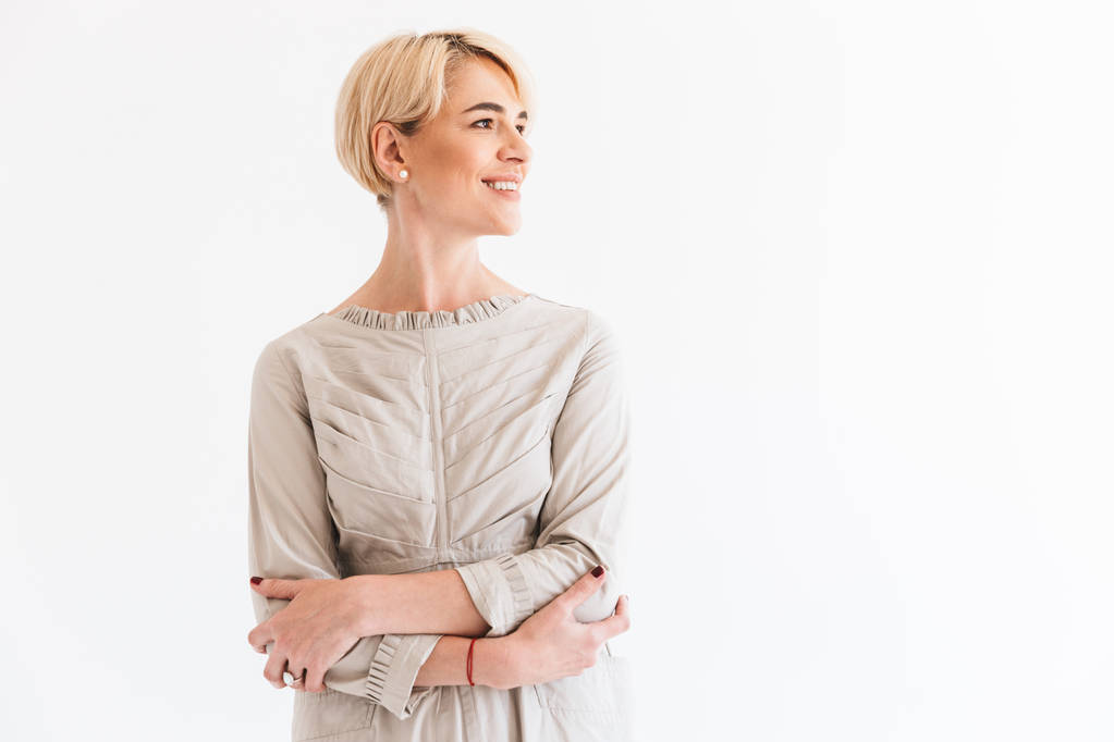 Image of charming blond middle aged woman looking aside at copyspace with beautiful smile and arms crossed isolated over white background in studio - Photo, Image