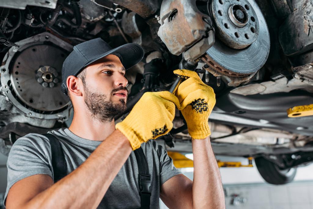 profesionální mechanik v uniformě opravy auto bez kol v dílně - Fotografie, Obrázek