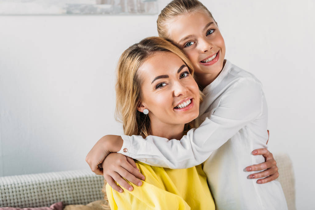mother and daughter embracing and looking at camera at home - Photo, Image