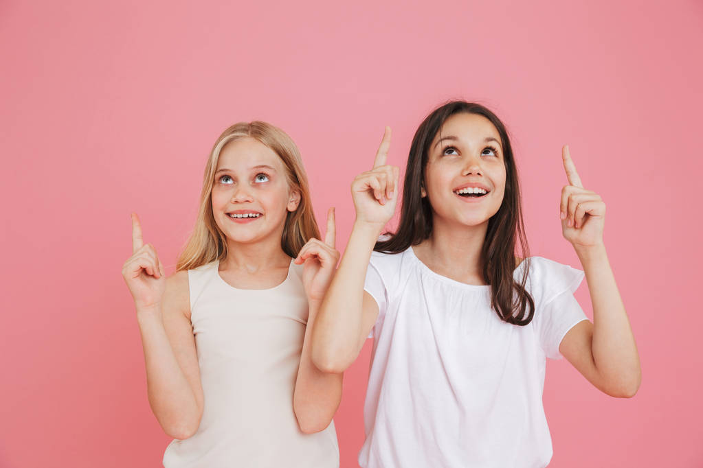 Photo de petites filles de 8 à 10 ans portant des vêtements décontractés pointant les doigts vers le haut vers l'espace d'écriture tout en regardant ensemble isolé sur fond rose
 - Photo, image