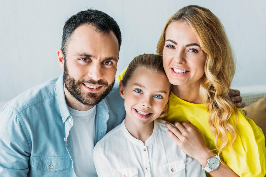 happy young family sitting on couch together and looking at camera - Photo, Image