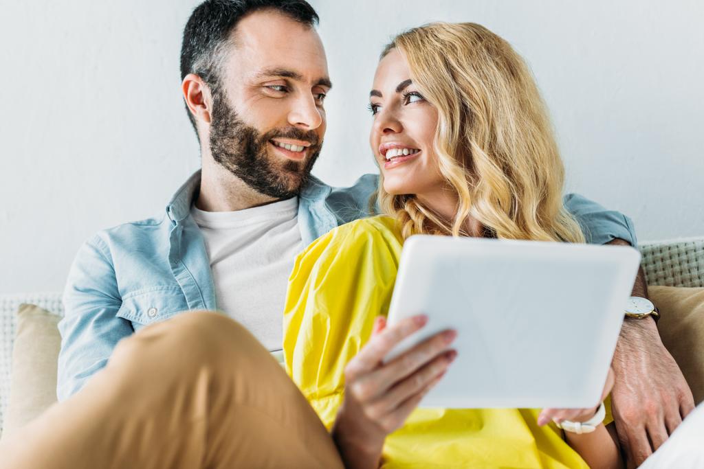 glückliches Paar nutzt gemeinsam Tablet, während es zu Hause auf der Couch sitzt - Foto, Bild