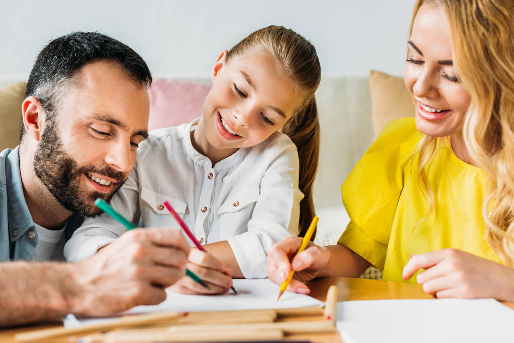 χαμογελαστός νεαρός οικογενειακό σχέδιο με μολύβια χρώματος μαζί στο σπίτι - Φωτογραφία, εικόνα