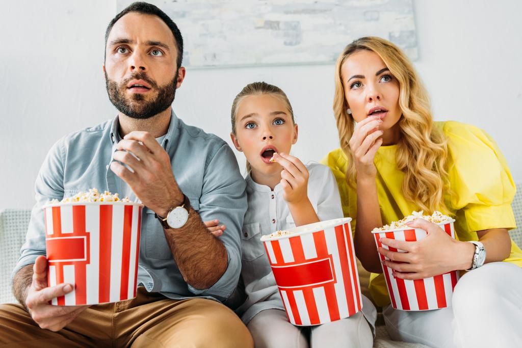 σοκαρισμένος νεαρή οικογένεια βλέποντας ταινία στο σπίτι με κουβάδες του ποπ κορν - Φωτογραφία, εικόνα