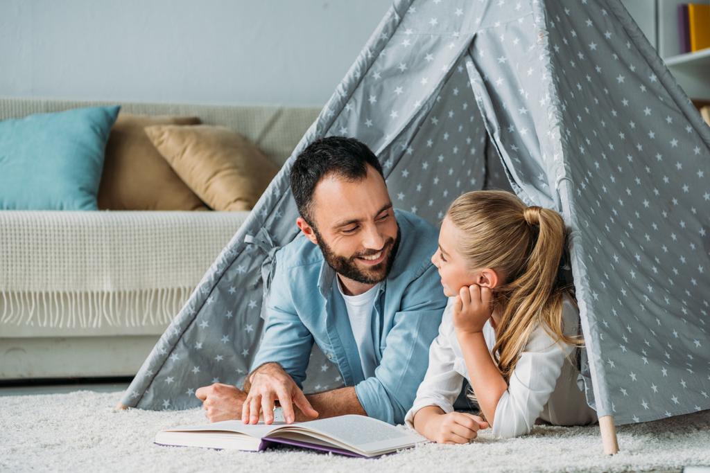 mutlu baba ve kızı yere teepee içinde yatan ve evde birlikte kitap okuma - Fotoğraf, Görsel