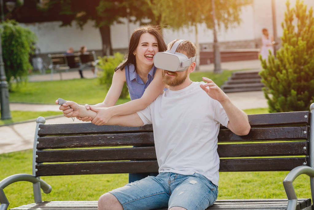 Καυκάσιος ζευγάρι παίζει ένα παιχνίδι χρησιμοποιώντας γυαλιά εικονικής πραγματικότητας στο δρόμο. VR ακουστικά. - Φωτογραφία, εικόνα