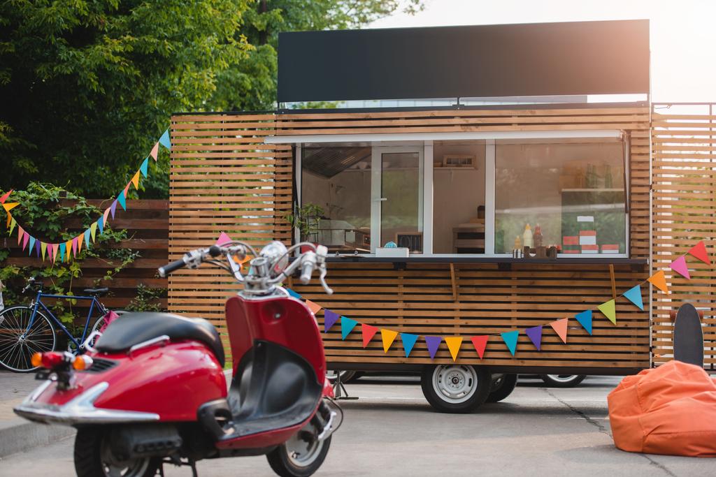 червоний скутер і харчова вантажівка з барвистими прапорами позаду
 - Фото, зображення