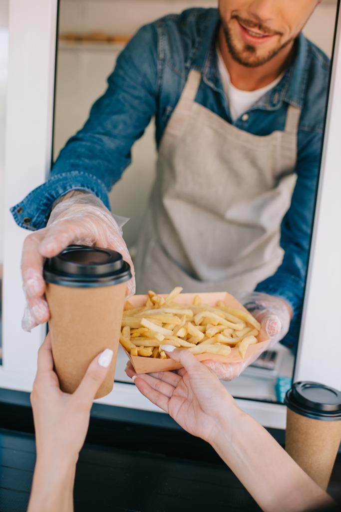 Schnappschuss von Koch, der Pommes frites und Kaffee an Kunden im Food-Truck verteilt - Foto, Bild