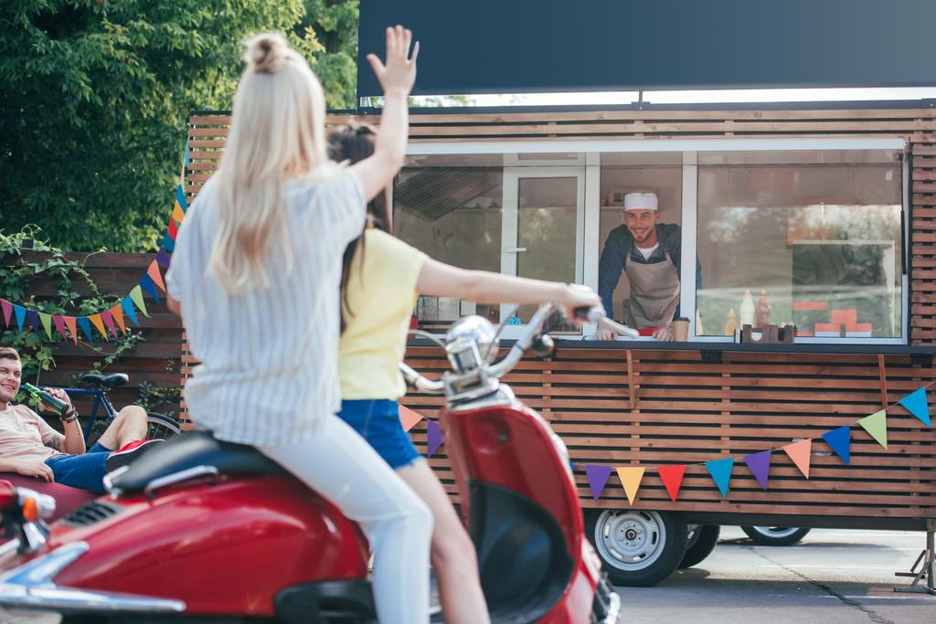 back view of girl on scooter waving hand to chef in food truck - Photo, Image