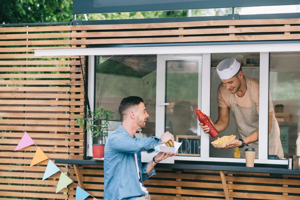 chef giving hot dog and ketchup to customer from food truck - Photo, Image