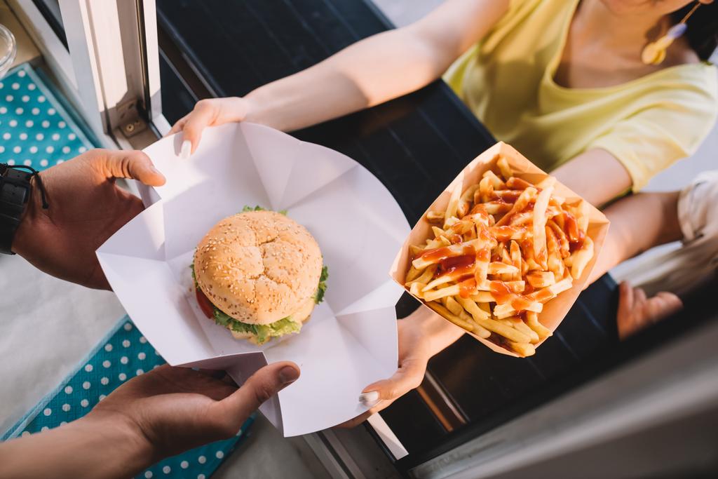 обрезанное изображение шеф-повара, дающего гамбургеры и картошку фри клиентам из фургона с едой
  - Фото, изображение
