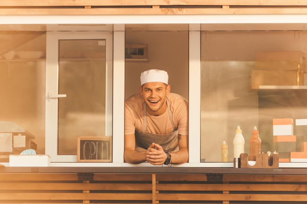 Lächelnd schaut der gut aussehende Koch von einem Food-Truck in die Kamera - Foto, Bild