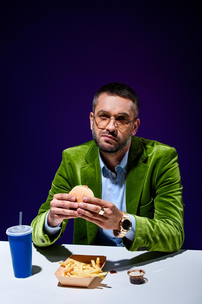 uomo in giacca di velluto mangiare hamburger a tavola con grida francesi e bibita gassata con sfondo blu
 - Foto, immagini