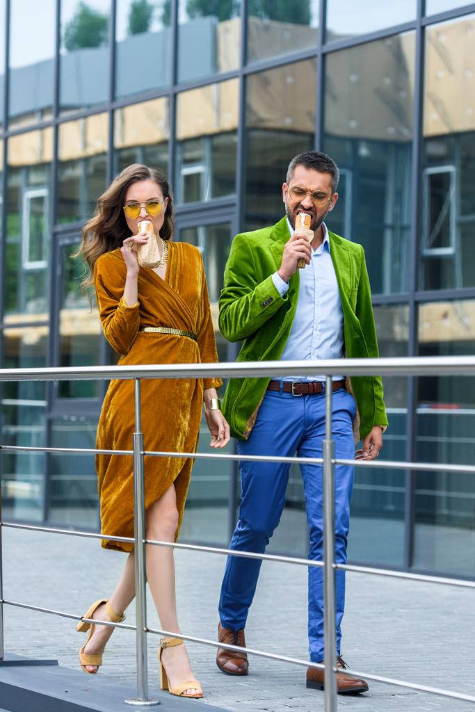pareja en traje de lujo comiendo perros calientes franceses mientras camina por la calle
 - Foto, Imagen