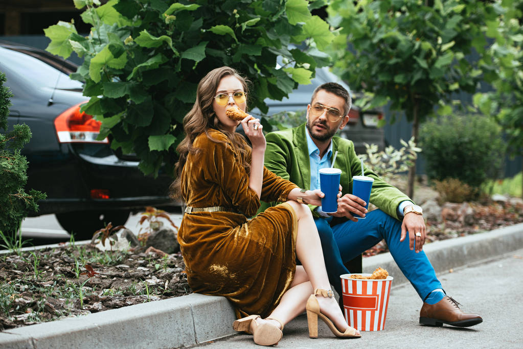 couple à la mode en vêtements de velours avec des jambes de poulet frit et des boissons dans la rue
 - Photo, image
