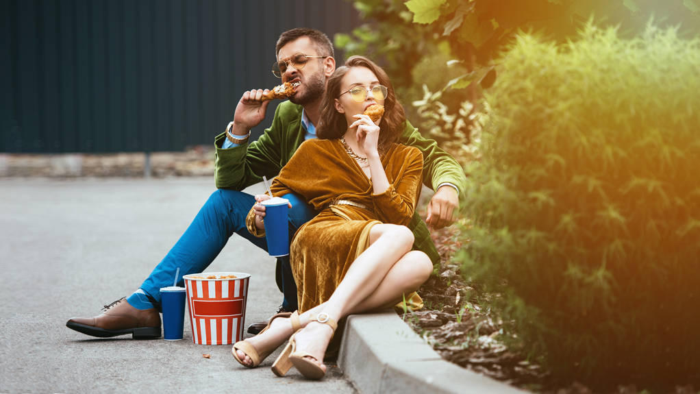 couple à la mode en velours manger des jambes de poulet frit dans la rue
 - Photo, image