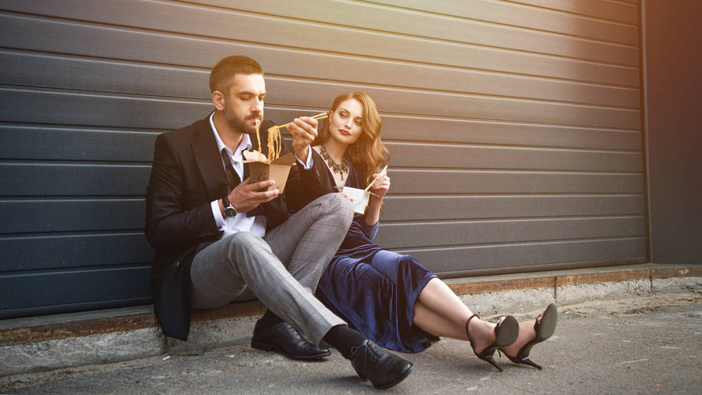 ζευγάρι σε μοντέρνα ρούχα με ασιατικές takeaway τρόφιμα που κάθεται στο δρόμο - Φωτογραφία, εικόνα