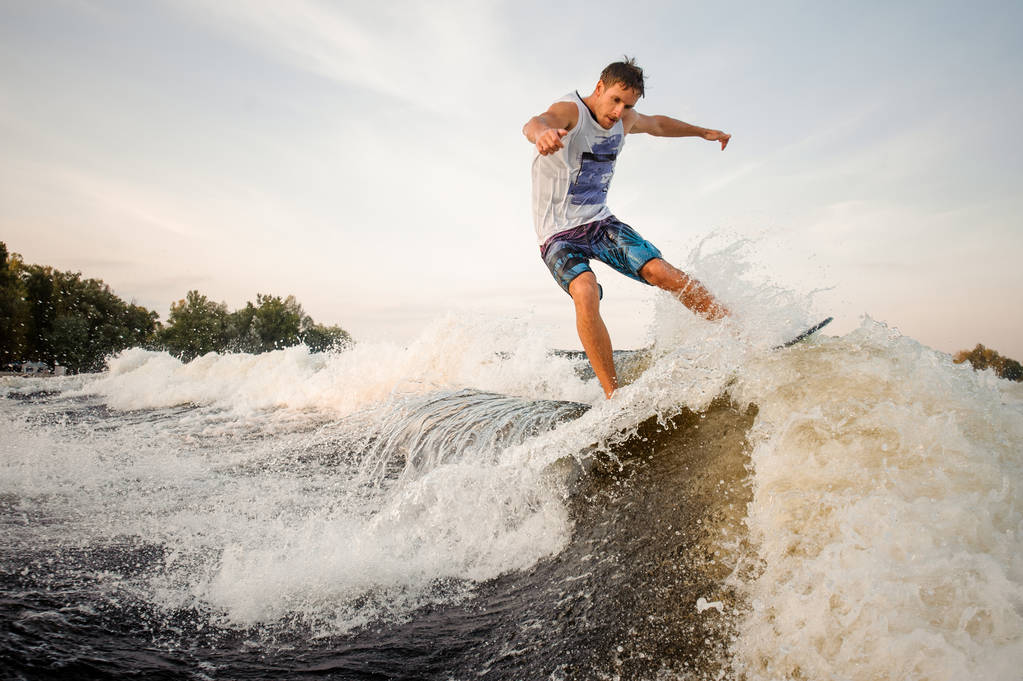 Muscular and strong wakesurfer jumping and riding down the river on the board against the background of clear sky - Photo, Image