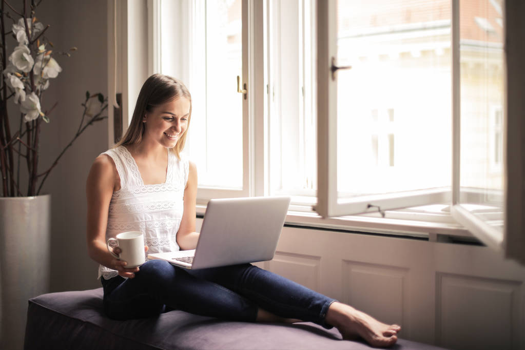 Młoda kobieta siedzi na kanapie i surfowanie w Internecie. - Zdjęcie, obraz
