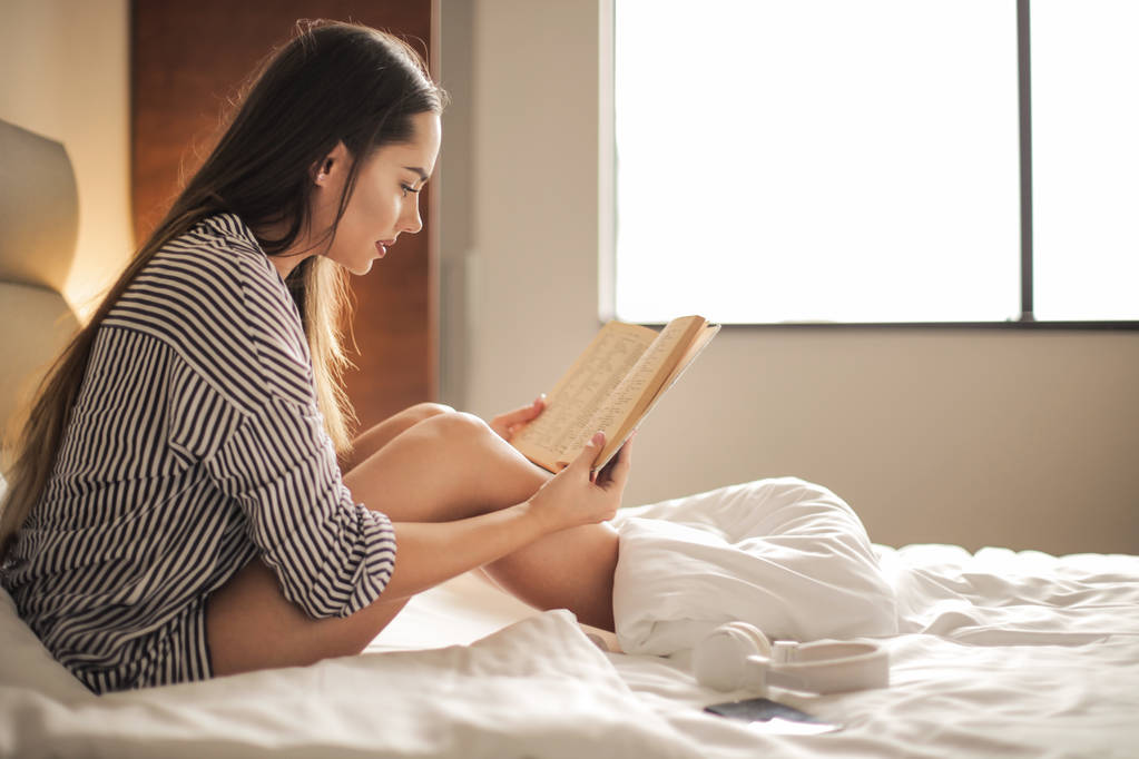 Nuori kaunis nainen lukee sängyssä. - Valokuva, kuva