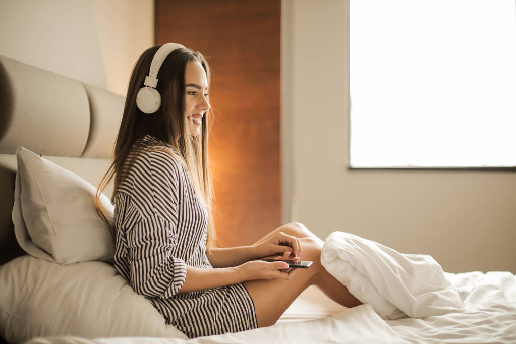 Young beautiful woman with headphones relaxing in bed. - Photo, Image