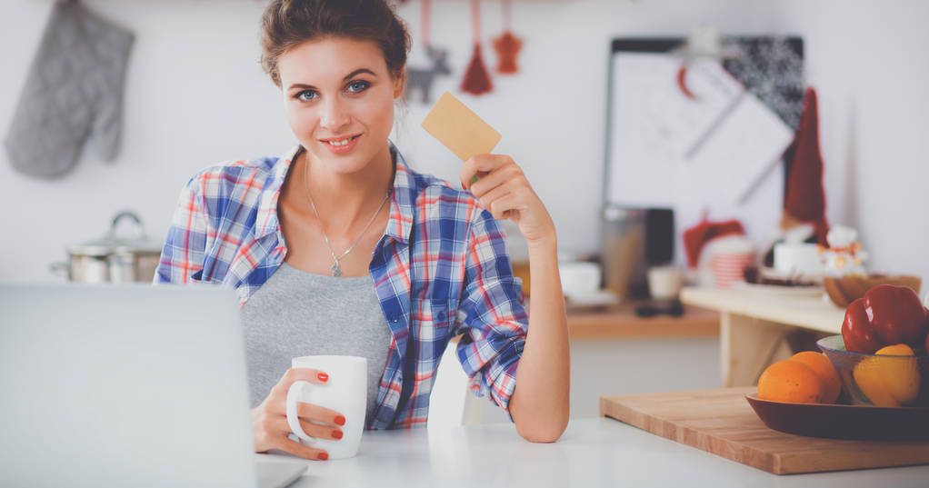 Χαμογελαστή γυναίκα online ψώνια χρησιμοποιώντας υπολογιστή και πιστωτική κάρτα στην κουζίνα - Φωτογραφία, εικόνα