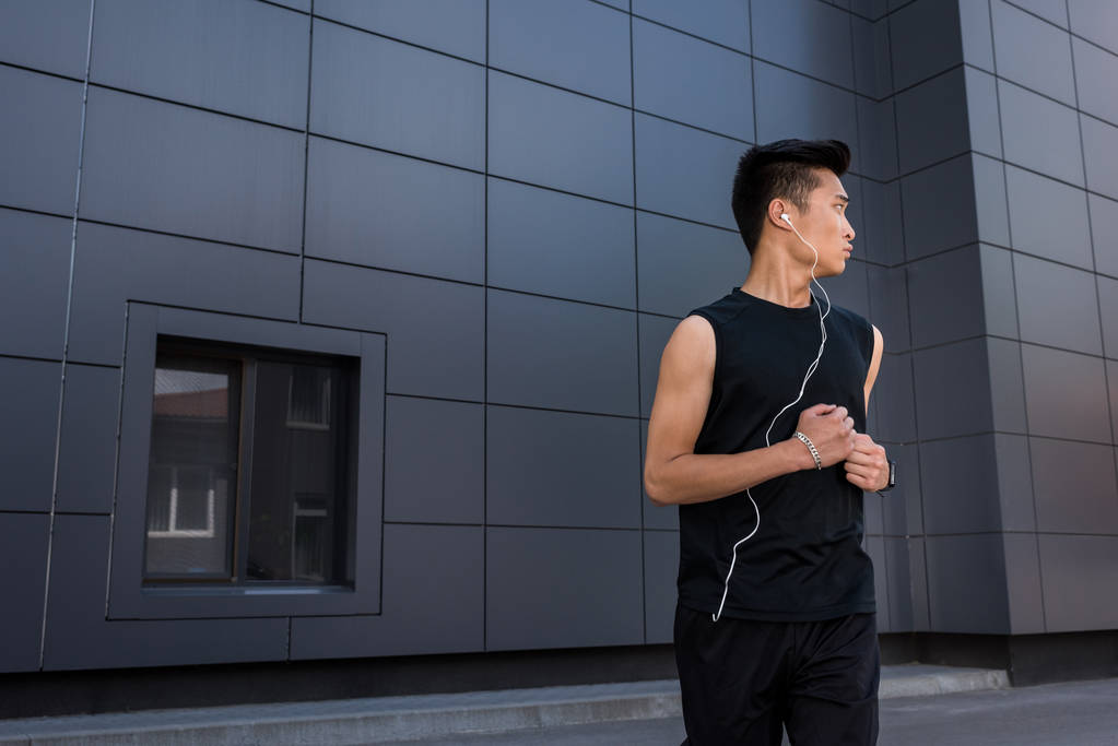 молодий азіатський спортсмен в навушниках, що працюють на міській вулиці
 - Фото, зображення