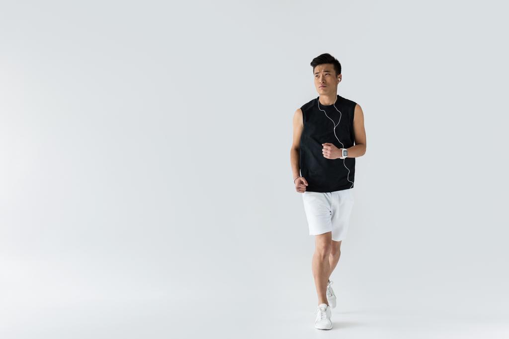 a fülhallgató a szürke háttérben futó komoly fiatal ázsiai sportember  - Fotó, kép