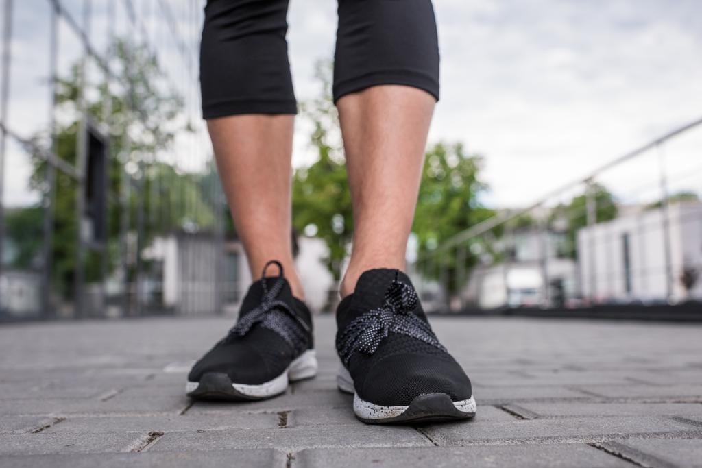 imagen recortada de las piernas de la deportista en zapatillas negras de pie en la calle
 - Foto, Imagen