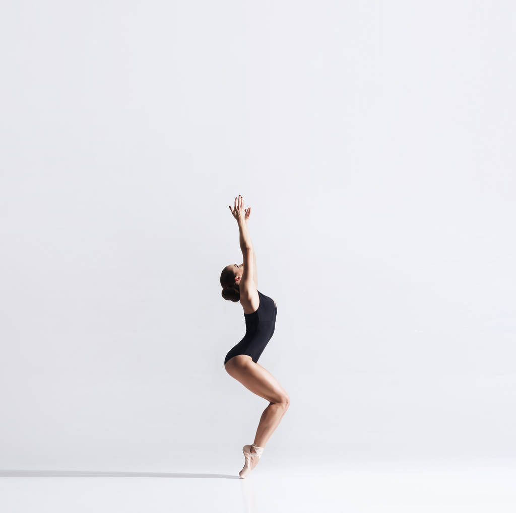 Bailarina en zapatos de punto y body está bailando en el estudio. Joven y elegante bailarina de ballet
. - Foto, Imagen