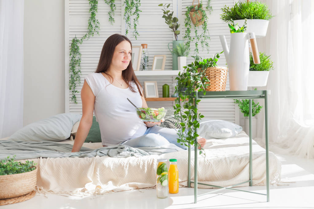 Молодая беременная женщина позирует в светлом современном скандинавском интерьере спальни
 - Фото, изображение