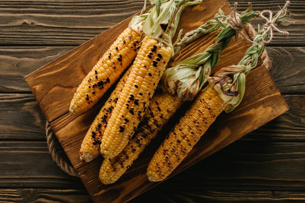 verhoogde weergave van heerlijk gegrild maïs op de snijplank op houten tafel  - Foto, afbeelding