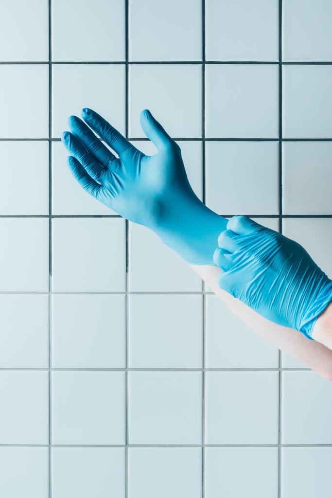 Oříznout záběr doktor nasadil modré gumové rukavice před bílých obkládačkách - Fotografie, Obrázek