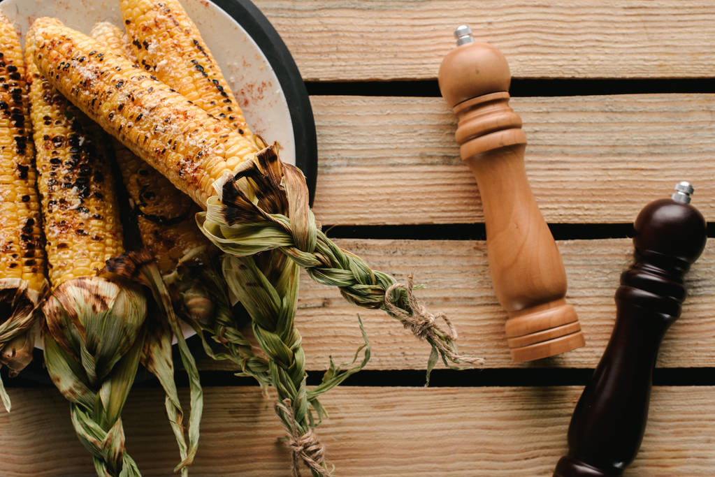 pohled shora grilované kukuřice na desce poblíž mlýnky na sůl a pepř na dřevěný stůl  - Fotografie, Obrázek